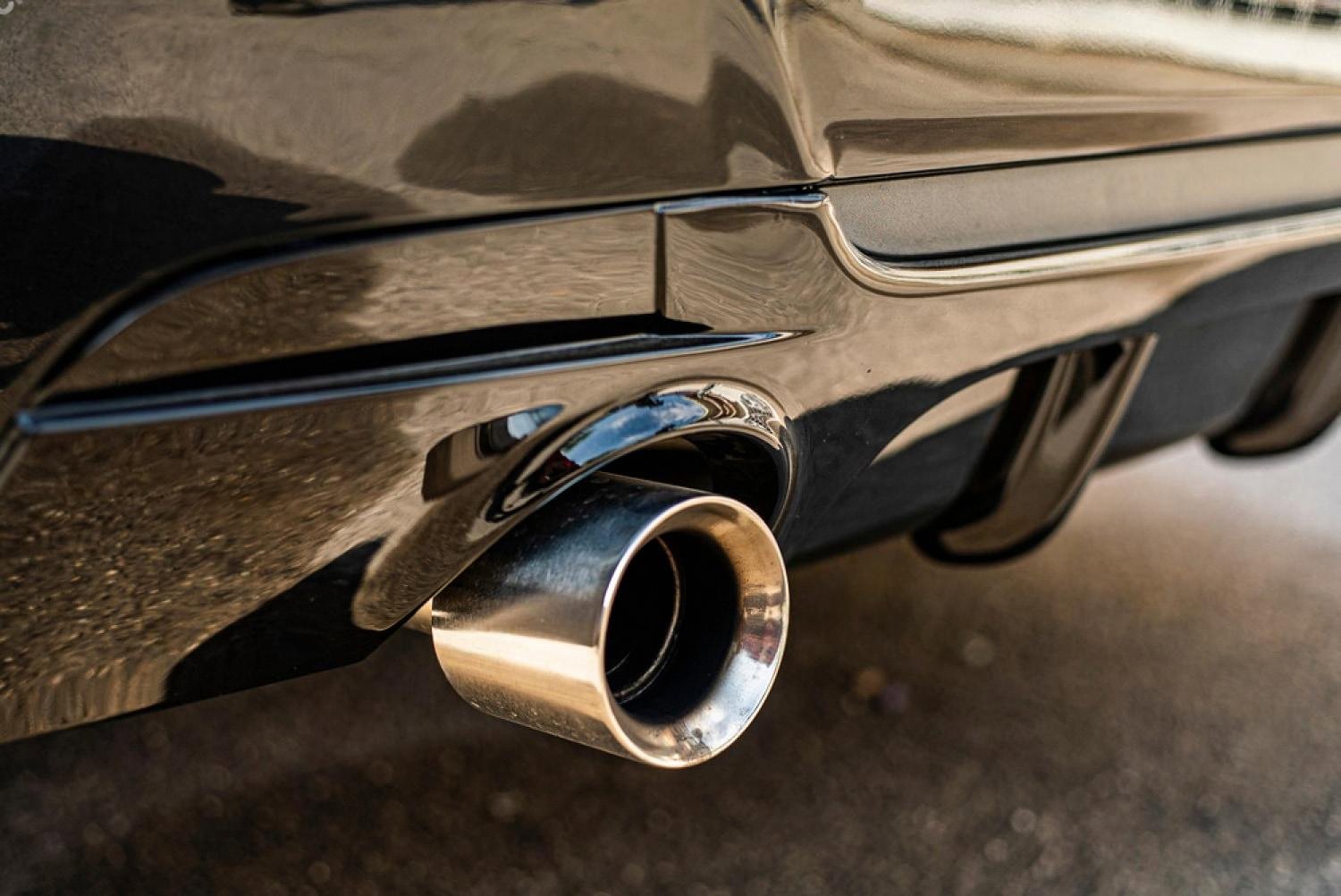 Close-up of a chrome car exhaust pipe on a black vehicle, a common source of cabin noise