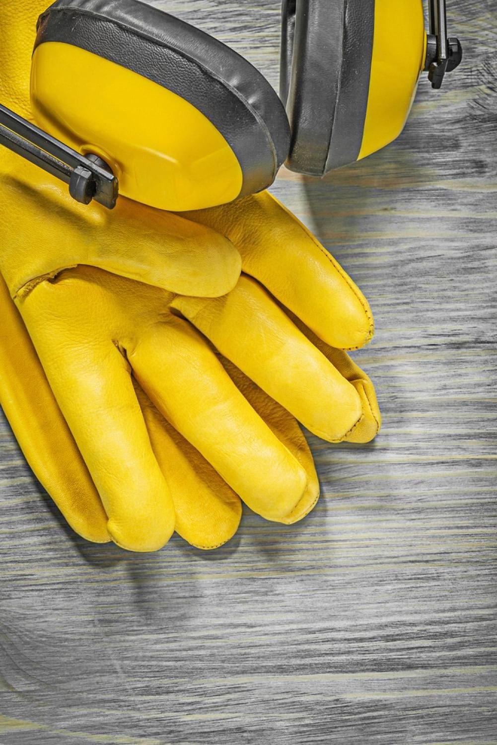 Yellow ear protection muffs and leather gloves laid on a wooden surface, tools used when soundproofing a car